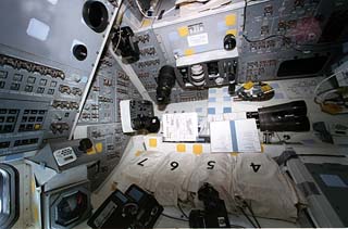 Mission specialist's station behind the commander's station, with cameras, binoculars and other items floating in the photo. 